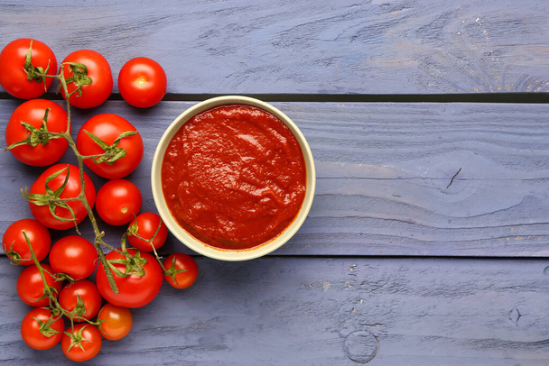 Bowl with tasty tomato paste and fresh vegetables on blue wooden background - Photo, Image