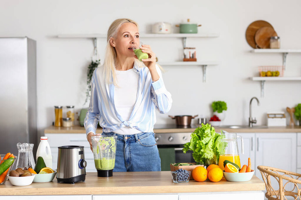 volwassen vrouw drinken gezonde smoothie in keuken - Foto, afbeelding