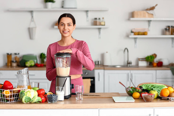 Sporty young woman making healthy smoothie with blender in kitchen - Photo, Image