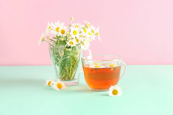 Copos de chá de camomila natural e flores na mesa turquesa perto da parede rosa - Foto, Imagem