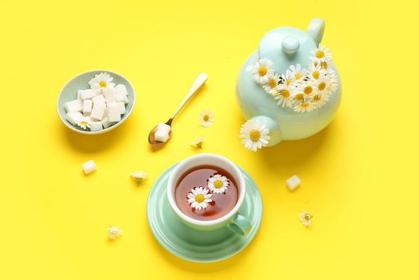 Bule com xícara de chá de camomila natural, cubos de açúcar e flores em fundo amarelo - Foto, Imagem