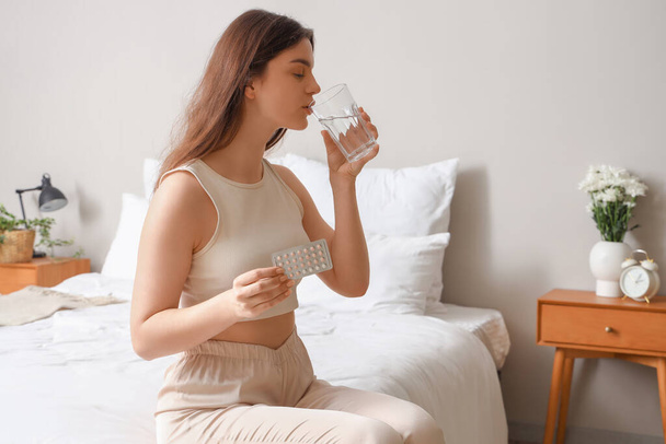 Mladá žena užívající antikoncepční pilulky se sklenicí vody v ložnici - Fotografie, Obrázek