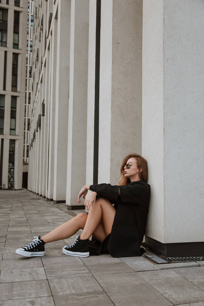 Portrait of a young beautiful woman in a jeans and jacket sitting on the steps of the outdoors. Attractive stylish hipster woman sitting on the stairs. girl wearing sunglasses  - Photo, Image