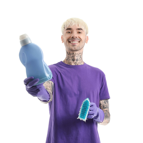 Joven hombre tatuado con botella de detergente y cepillo de limpieza sobre fondo blanco - Foto, imagen