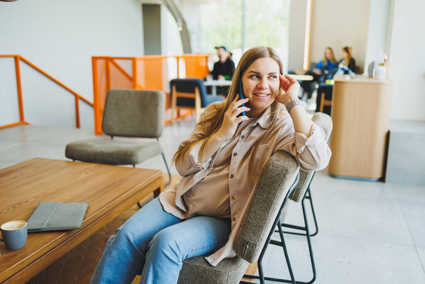 Ženské studentky sedí na pohovce v kavárně s kávou a telefonují. Vzdálená práce online v útulné kavárně - Fotografie, Obrázek