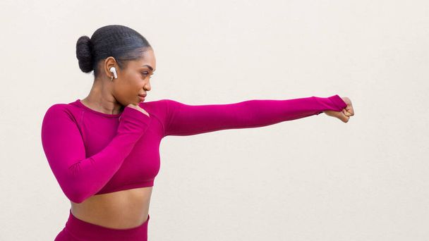Vista laterale di forte atletica giovane donna nera in abbigliamento sportivo rosa facendo calci su sfondo bianco muro vuoto, signora afro-americana praticare arti marziali karate, autodifesa, panorama, spazio copia - Foto, immagini