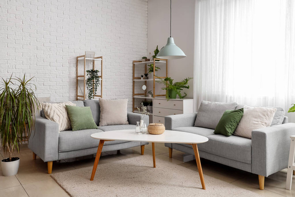 Belső tér világos nappali hangulatos szürke kanapék, dohányzóasztal és szobanövények - Fotó, kép