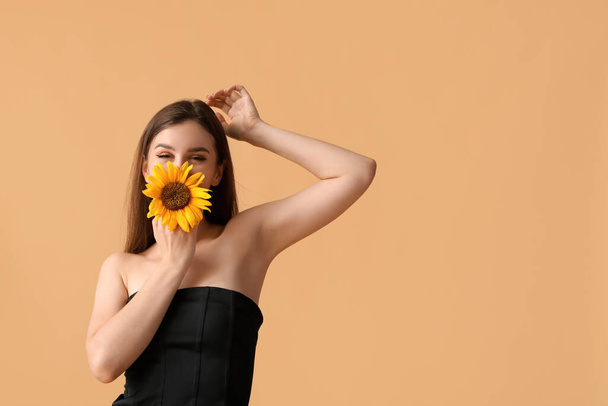 Junge Frau mit schöner Sonnenblume auf orangefarbenem Hintergrund - Foto, Bild