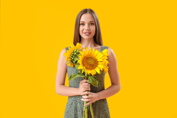 Jonge gelukkige vrouw met boeket van mooie zonnebloemen op gele achtergrond - Foto, afbeelding