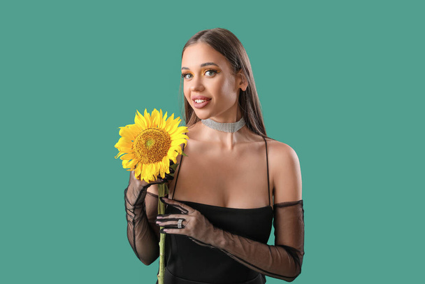 Elegant happy young woman with beautiful sunflower on green background - Photo, Image