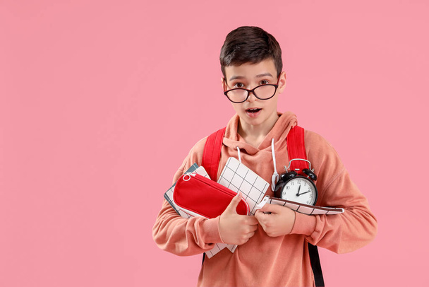 Portrait of shocked schoolboy with school supplies and alarm clock on pink background - Photo, Image