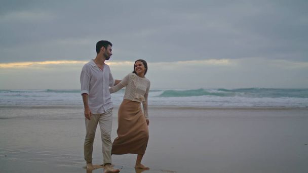 Счастливые возлюбленные гуляющие по вечернему пляжу. Испанская пара наслаждается океанским побережьем снаружи. Два романтических любовника бегают на свидание на природе. Улыбающиеся супруги проводят время вместе. Концепция отдыха - Фото, изображение