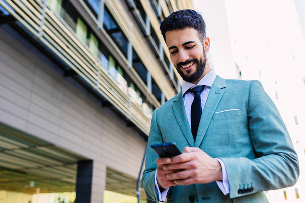 外の建物オフィスに立っている携帯電話を使用して正式なスーツの専門のビジネスマン. スマートフォンを持っているスマートフォンの笑顔起業家セールスマン. テクノロジーとビジネスコンセプト. - 写真・画像