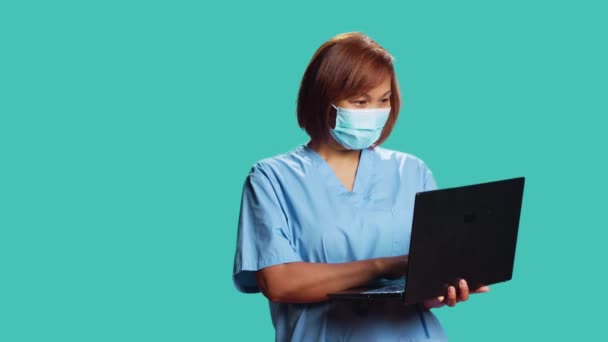 Крупним планом медсестра спілкується з пацієнтом на ноутбуці під час онлайн-телевізійної перевірки здоров'я. Щасливий експерт з охорони здоров'я ізольований над студійним фоном за допомогою гаджета, в медичній масці для обличчя
 - Кадри, відео