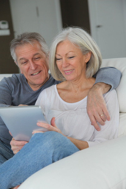 Senior couple sitting in sofa with electronic tablet - Fotoğraf, Görsel