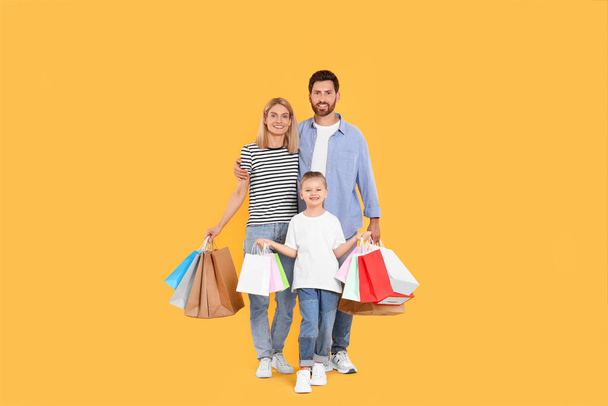 Family shopping. Happy parents and daughter with paper bags on orange background - Foto, Imagen