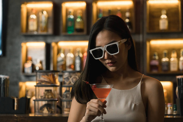 Asijské žena pití koktejl na baru, zatímco nosí sluneční brýle. - Fotografie, Obrázek
