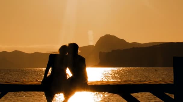 Mężczyzna i kobieta siedzi na most na zachodzie słońca - Materiał filmowy, wideo