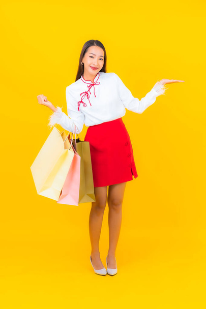 Portrét krásná mladá asijská žena s nákupní taškou a kreditní kartou na žlutém pozadí - Fotografie, Obrázek