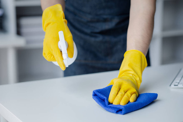 Person cleaning the room, cleaning staff is using cloth and spraying disinfectant to wipe the tables in the company office room. Cleaning staff. Maintaining cleanliness in the organization. - Photo, Image
