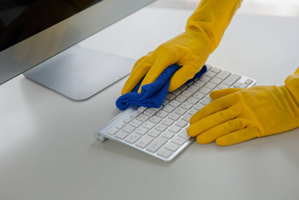 Persona sala de limpieza, trabajador de limpieza está utilizando tela para limpiar el teclado de la computadora en la sala de oficina de la empresa. Personal de limpieza. Concepto de limpieza en la organización. - Foto, imagen