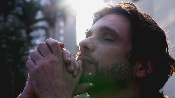 Faithful young man looking up at sky in prayer asking for God_s help with hopeful expression. A Spiritual male person in 30s with lens flare sunlight - Photo, Image