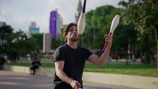 Erkek jonglör şehir parkında yeteneklerini sergiliyor. Havada nesneleri hokkabazlık yapan sanatçı - Fotoğraf, Görsel