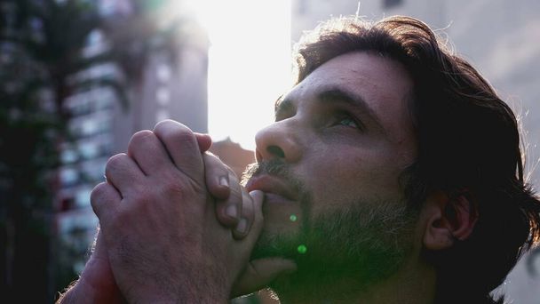 信心深い若者は祈りの中で空を見上げ,希望に満ちた表情で神に助けを求める. 30代のスピリチュアルな男性,レンズフレアの日光 - 写真・画像