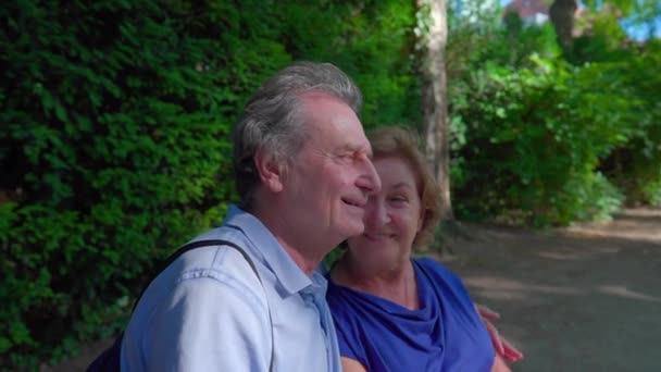 Radosna para seniorów ciesząca się słonecznym dniem w parku. Mąż objął starszą żonę uśmiechem i śmiechem na świeżym powietrzu, szczęśliwym małżeństwem - Materiał filmowy, wideo