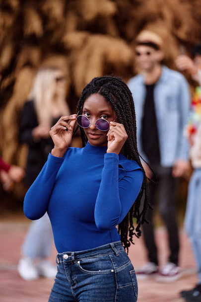 Sebevědomá Afroameričanka se slunečními brýlemi dívá do kamery, zatímco pózuje venku na večírku. - Fotografie, Obrázek