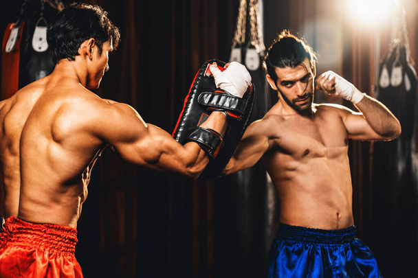 Le boxeur asiatique et caucasien Muay Thai déchaîne le punch lors d'une séance d'entraînement de boxe féroce, offrant une frappe de poinçon à l'entraîneur de sparring, mettant en valeur la technique et les compétences de boxe thaïlandaise Muay. Impulsion - Photo, image