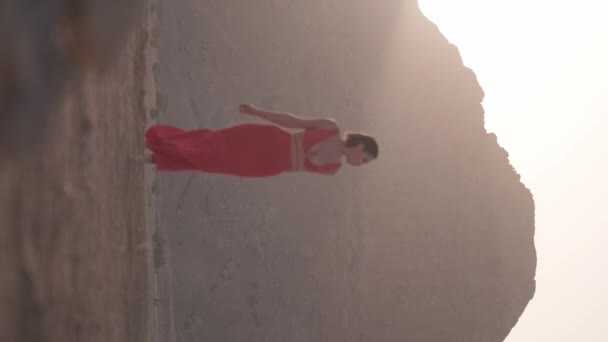 Вертикальный портрет молодой женщины в длинном платье, идущей босиком по песку пустыни на фоне заходящего солнца. Slow Motion. - Кадры, видео