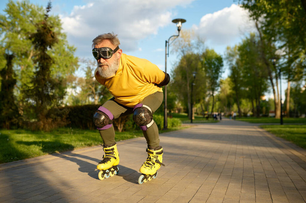 Senior man wearing funny goggles enjoying speed ride on roller skates over city park background - 写真・画像