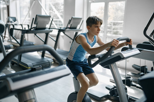 Active teenager boy doing cardio training on orbitrek at gym. Healthy and sports lifestyle for children - Photo, Image