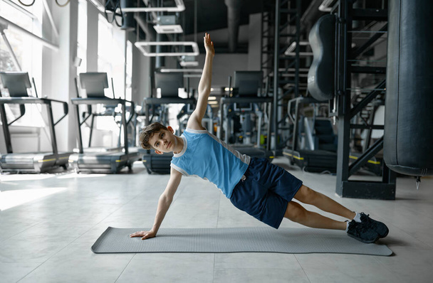 Adolescente fitness chico de pie en tablón lateral haciendo entrenamiento de núcleo en el club de gimnasia. Deporte e infancia - Foto, imagen