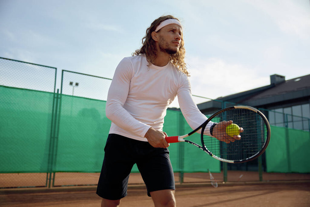 Сконцентрированный теннисист с ракеткой и тренировками по мячу на открытой площадке. Подготовка к службе - Фото, изображение