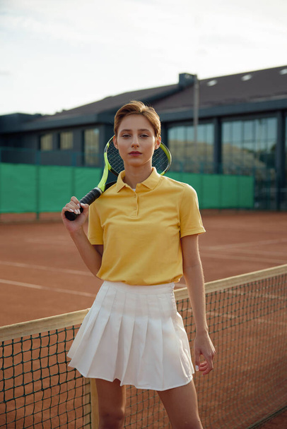Young woman tennis player wearing trendy fashion sportswear posing with racket at net. Leisure activity and sport outdoors concept - Photo, Image