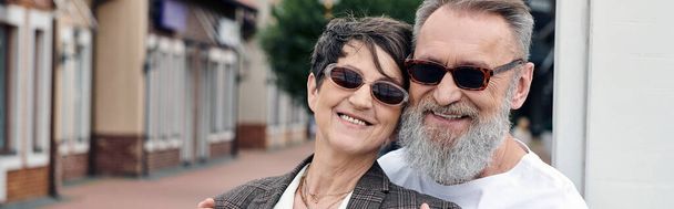 šťastný, starší pár v slunečních brýlích s úsměvem a pohledem na kameru, léto, starší muž objímající ženu - Fotografie, Obrázek