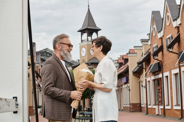 coppia anziana positiva in occhiali da sole, uomo guardando donna con fiori, estate, bouquet, romanticismo - Foto, immagini