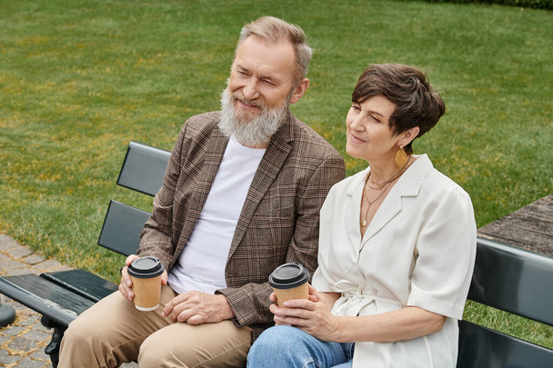 heureux homme et femme âgés assis sur le banc, tenant des tasses en papier avec café, couple âgé, romance - Photo, image