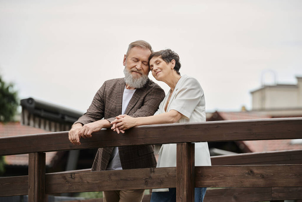 щаслива пара, що стоїть разом на мосту, літня любов, бородатий чоловік і жінка з закритими очима - Фото, зображення