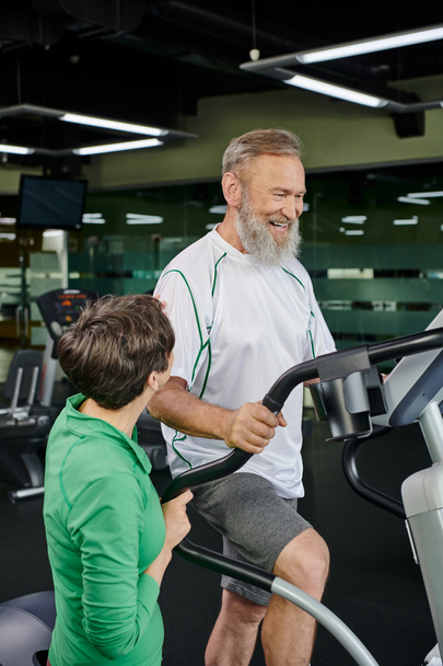 happy and bearded senior man exercising near woman in gym, husband and wife, active seniors, sport - Photo, Image