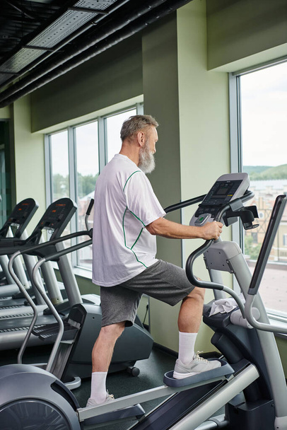bearded senior man working out on stepper exercise machine, elderly in gym, active senior, sport - Photo, Image