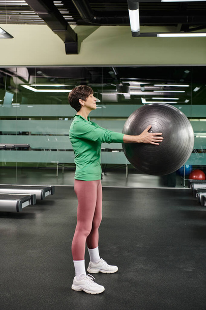 femme âgée faisant de l'exercice avec balle de fitness en salle de gym, senior actif, fitness et sport, vue latérale - Photo, image