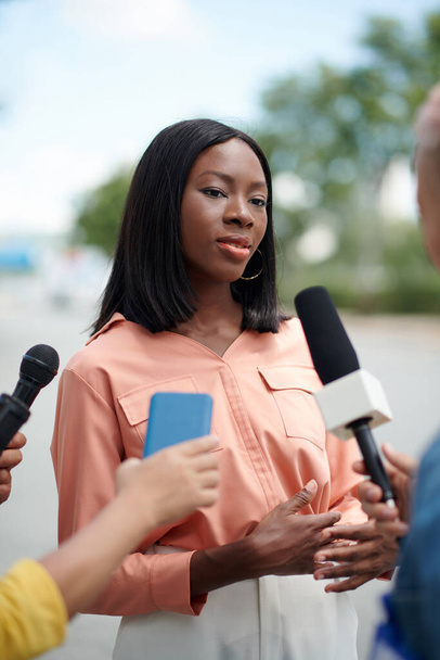 Porträt einer eleganten schwarzen Frau, die im Freien mit Journalisten spricht - Foto, Bild