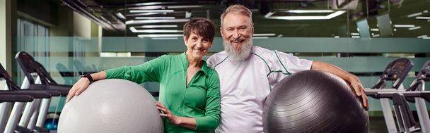 deportivo pareja de ancianos, feliz hombre y mujer sosteniendo pelotas de fitness, personas mayores activas en el gimnasio, pancarta - Foto, imagen