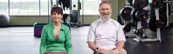 feliz pareja de ancianos sentado y mirando a la cámara en el gimnasio, personas mayores activas, estilo de vida saludable, pancarta - Foto, imagen