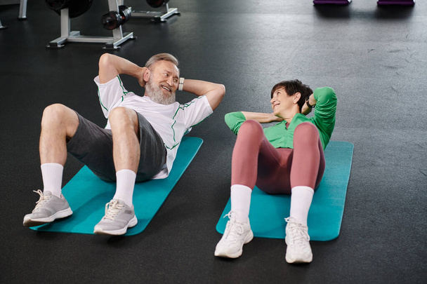 elderly man and woman doing sit ups, active seniors exercising on fitness mats in gym, healthy life - Photo, Image