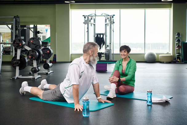 elderly man stretching back near happy woman, fitness mats, active seniors, vibrant and healthy - Photo, Image