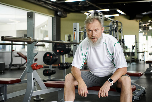 homme âgé fatigué avec barbe regardant la caméra après l'entraînement, machine d'exercice dans la salle de gym, athlète - Photo, image